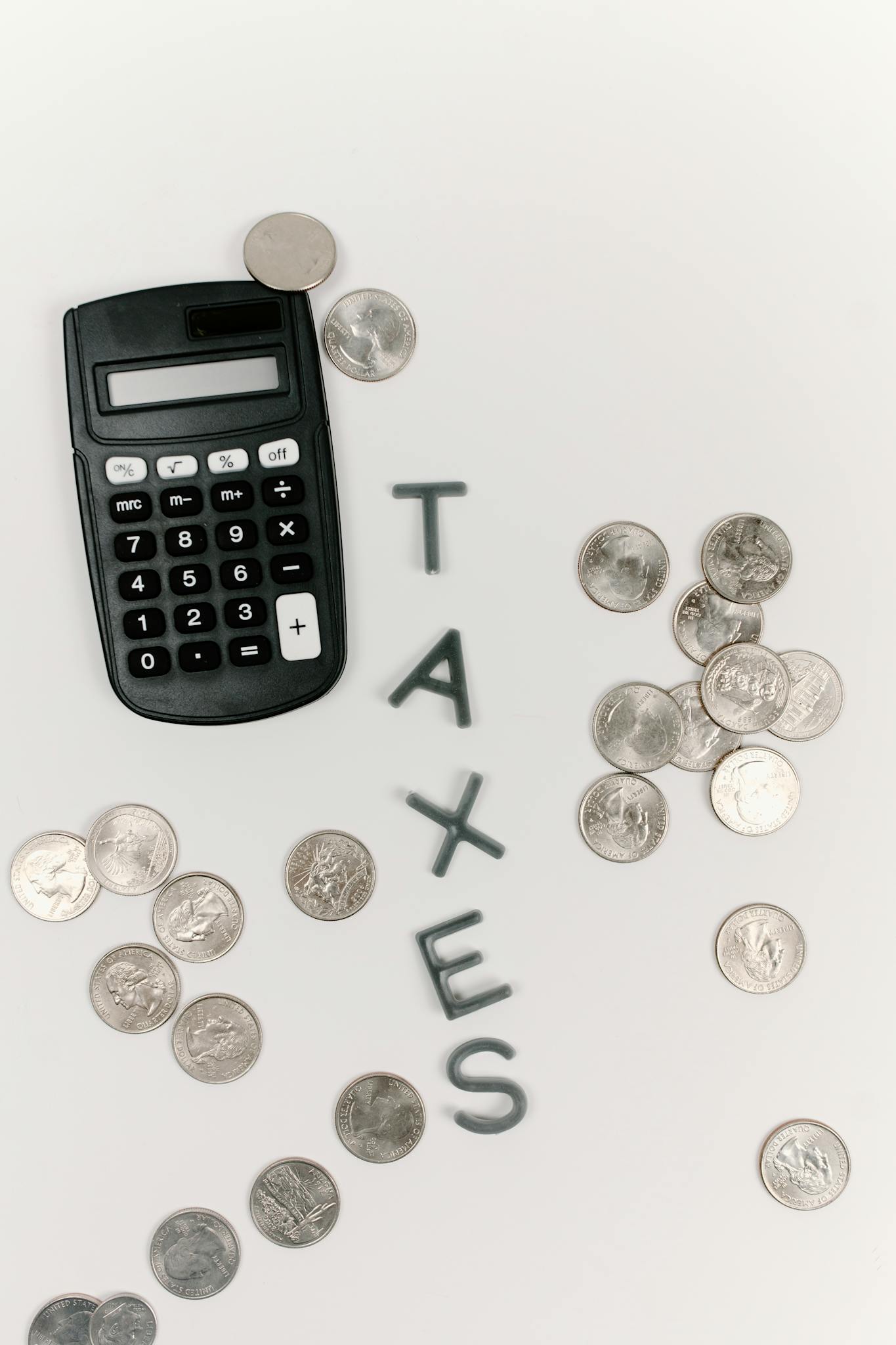 Calculator and scattered coins with the word 'TAXES' on a white background.